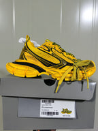 Side profile of the sneaker resting on a gray shoe box; the box label shows yellow/black color details and size C 37.