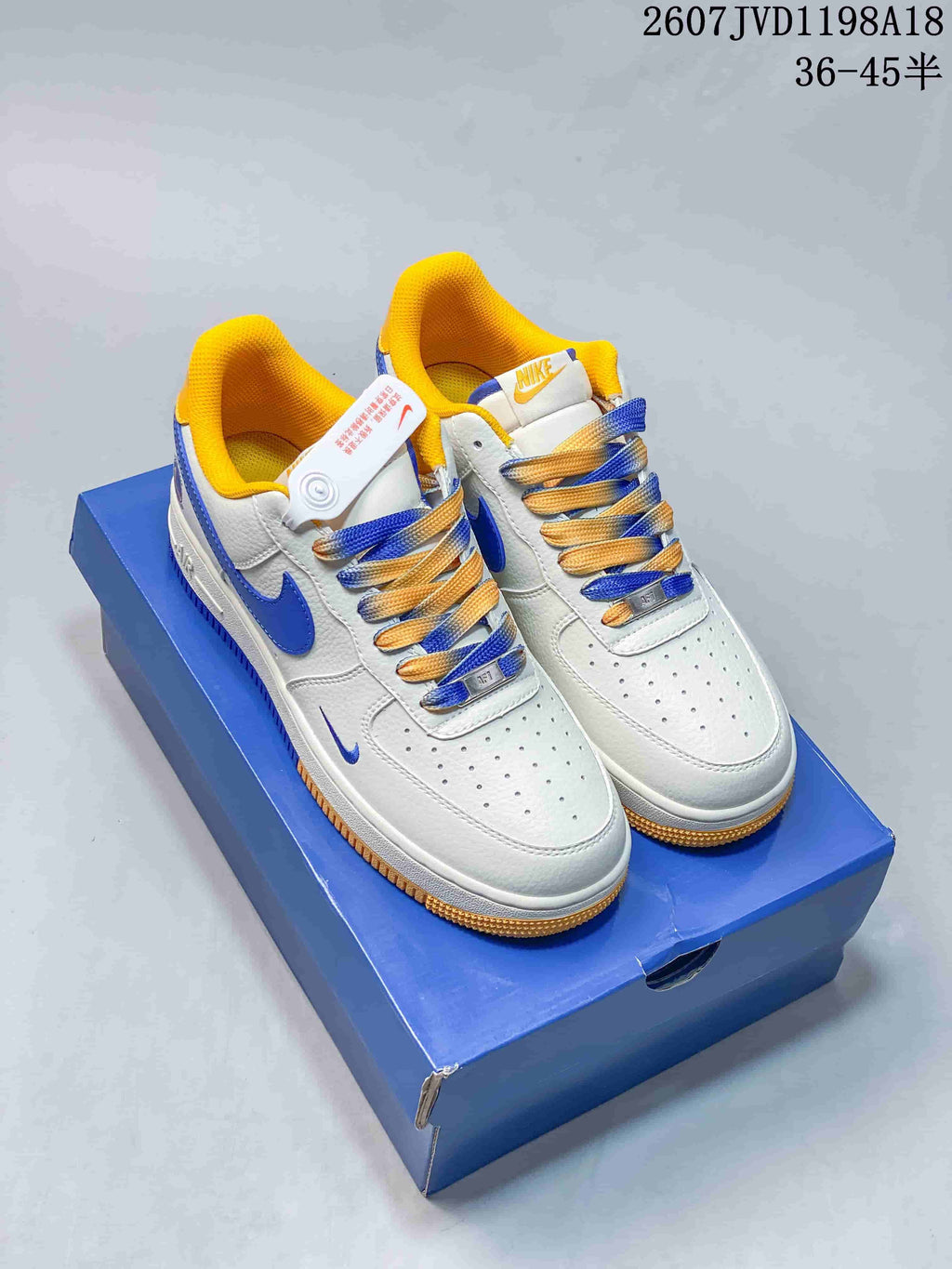 Pair of white sneakers with blue and yellow accents, multicolor laces, and a blue shoebox.