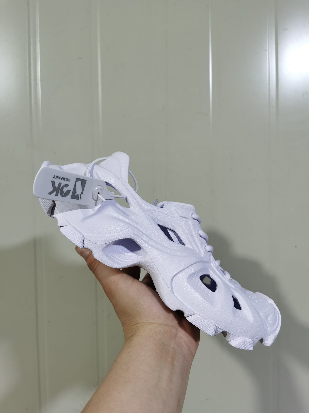 White open-panel sneaker held at an angle, showing sculpted side cutouts and a chunky outsole.