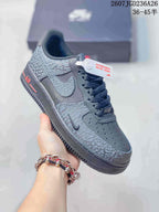 Angled side view of the dark gray sneaker with patterned overlays, swoosh detail, red heel-side accent, and lace closure.