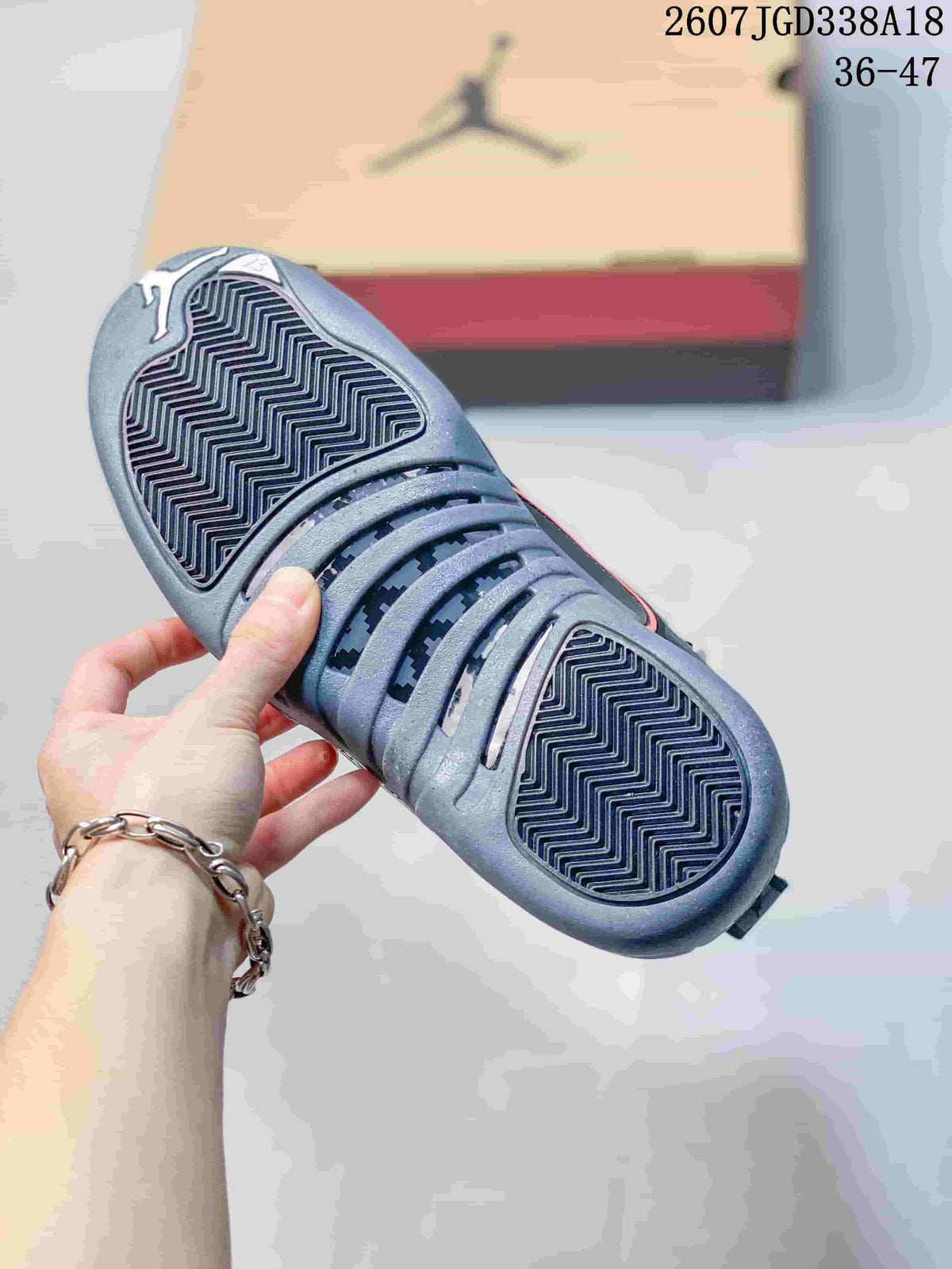 Close view of the sneaker outsole showing a repeating zigzag traction pattern and the shoebox in the background.