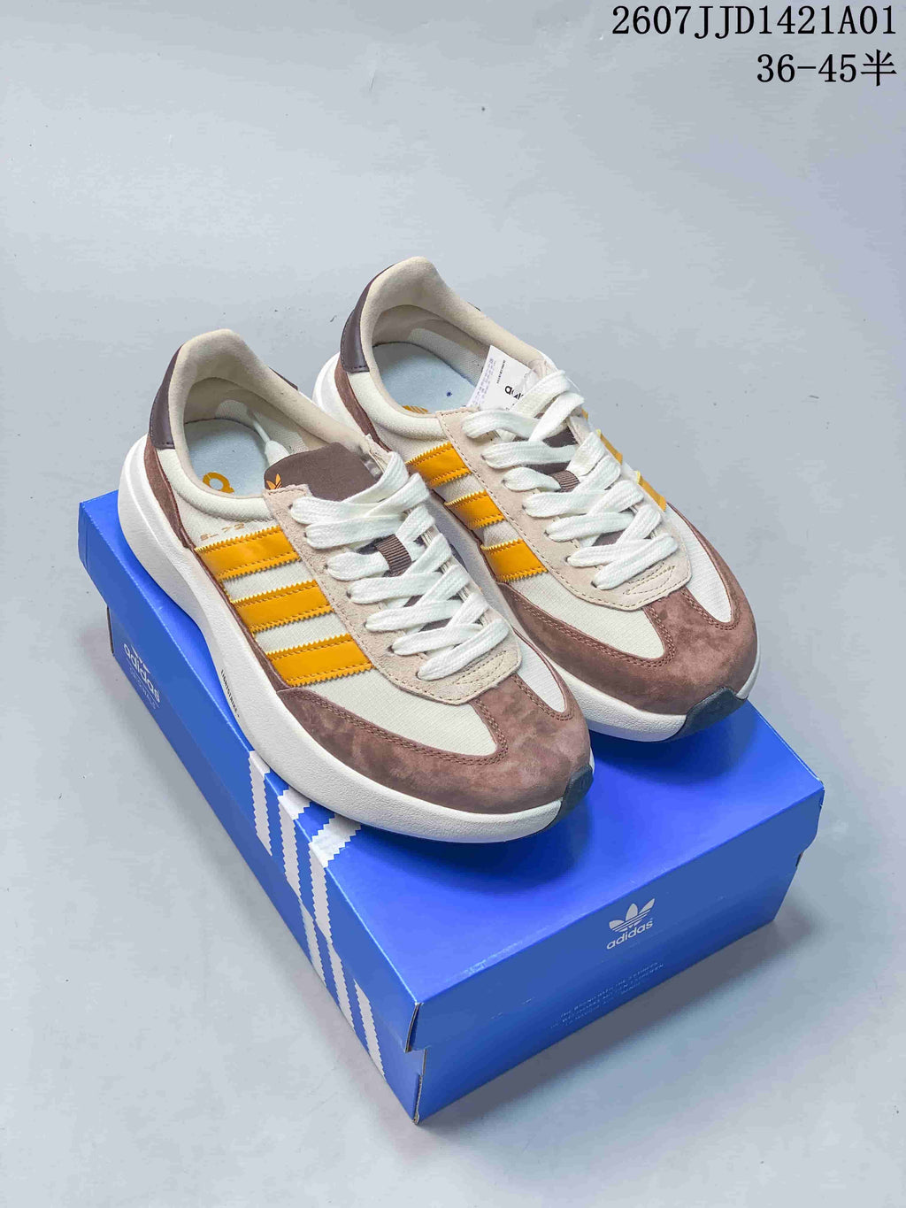 Pair of off-white, taupe, and yellow Adidas retro sneakers on a blue box