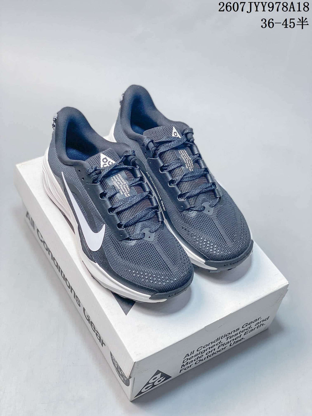 Pair of dark gray and white Nike ACG Pegasus Trail sneakers displayed on an ACG shoe box.