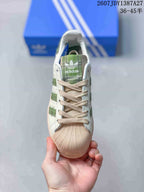 Front view showing the beige shell-toe style front, beige laces, green tongue detail, and white upper.