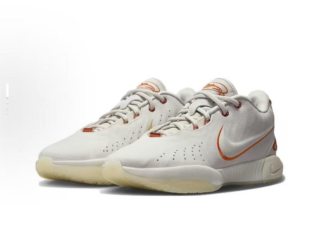 White low-top Nike basketball shoes with orange accents, shown as a pair.
