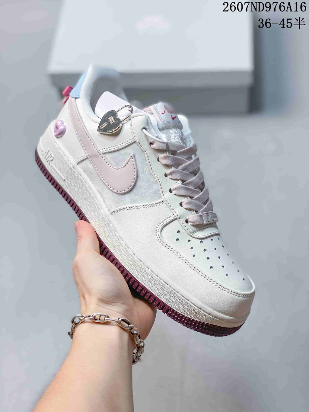 Angled side view showing the white sneaker, pale pink Swoosh, heart-shaped charm and dark pink outsole.