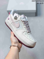 Angled side view showing the white sneaker, pale pink Swoosh, heart-shaped charm and dark pink outsole.