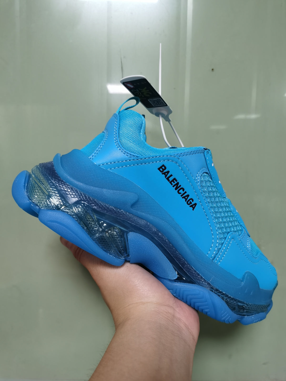 Angled view of a cyan blue Balenciaga sneaker with visible side branding, mesh details, and a transparent-look structured sole.