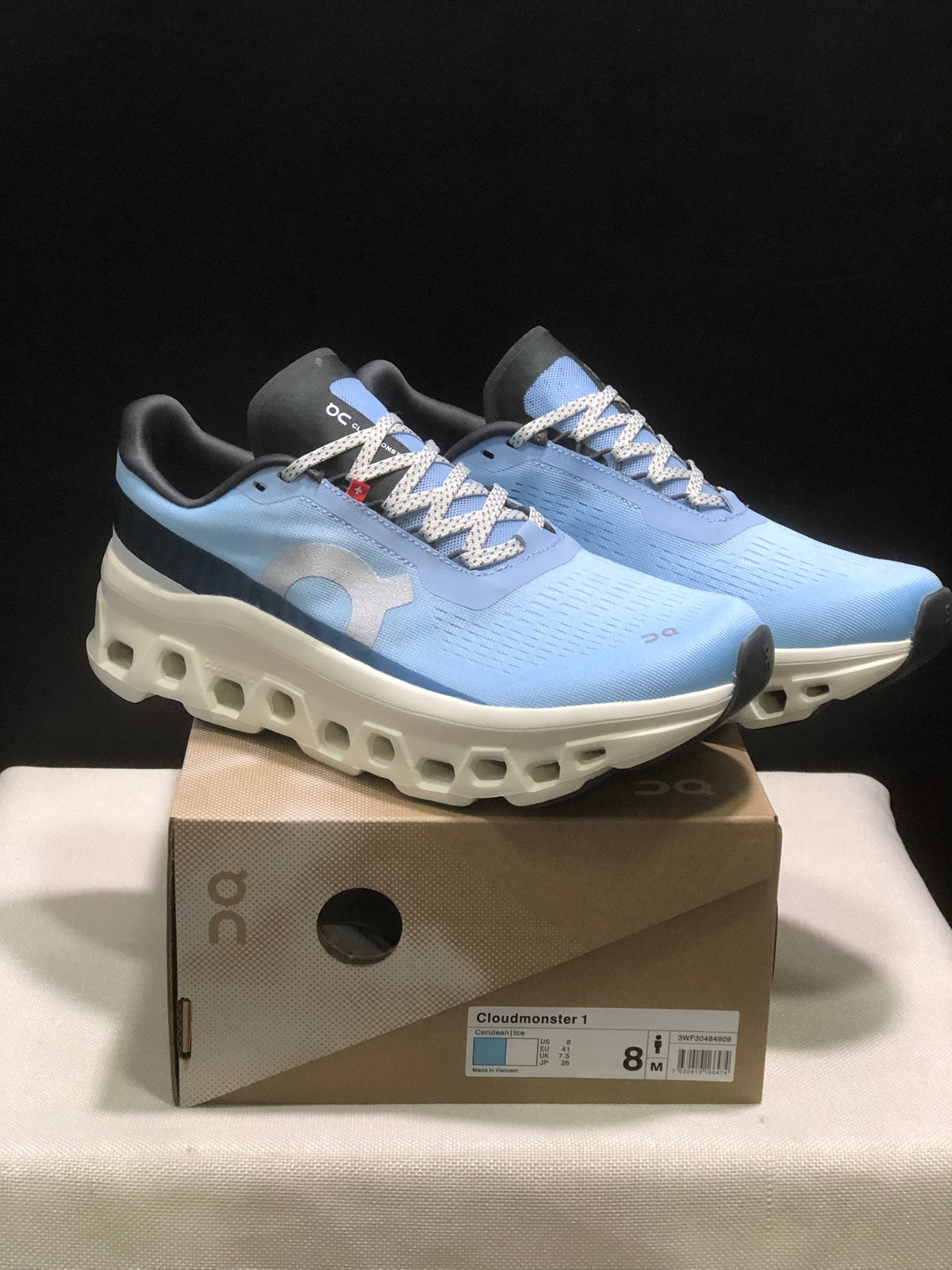 Pair of light blue and white On Cloudmonster 1 sneakers displayed on the product box; the box label shows an EU 42 sample size.