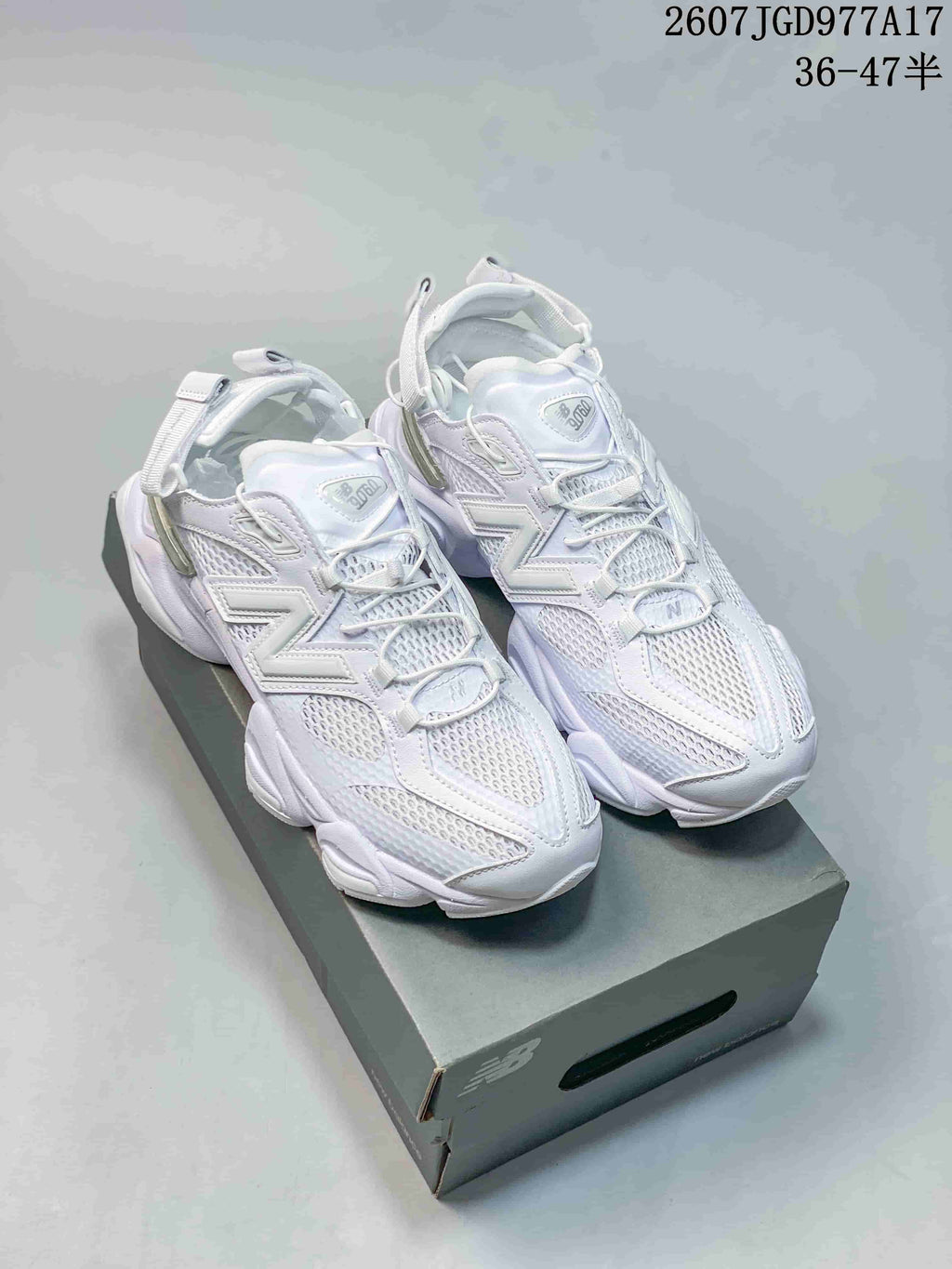 Pair of predominantly white New Balance 9060 sneakers displayed on a shoebox, showing the chunky sole and adjustable heel straps.
