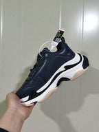 Side view of a dark blue-grey Balenciaga Triple S sneaker showing layered white and black sole details and a textured outsole.