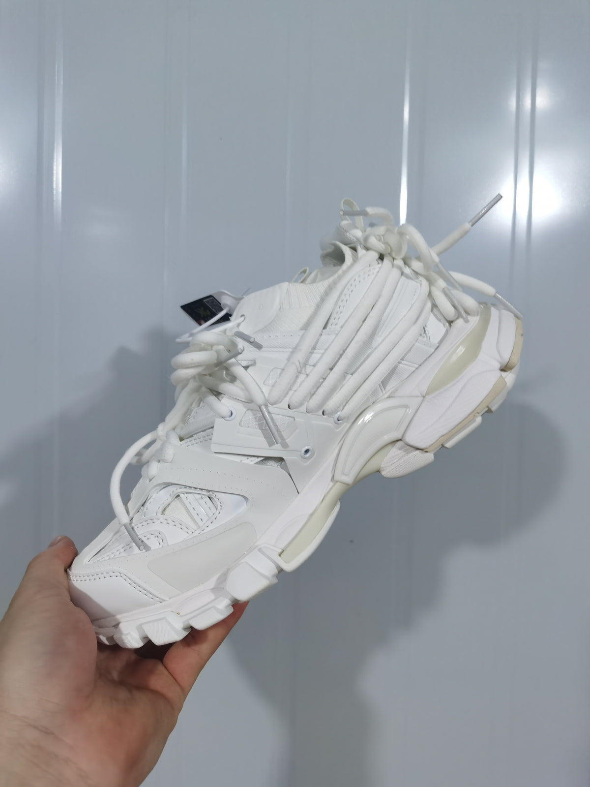 Top and side view of the white sneaker highlighting its layered panels, multiple laces, and sculpted outsole.