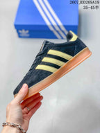 Side profile of the black low-top sneaker with gold stripes and a gum-colored sole.