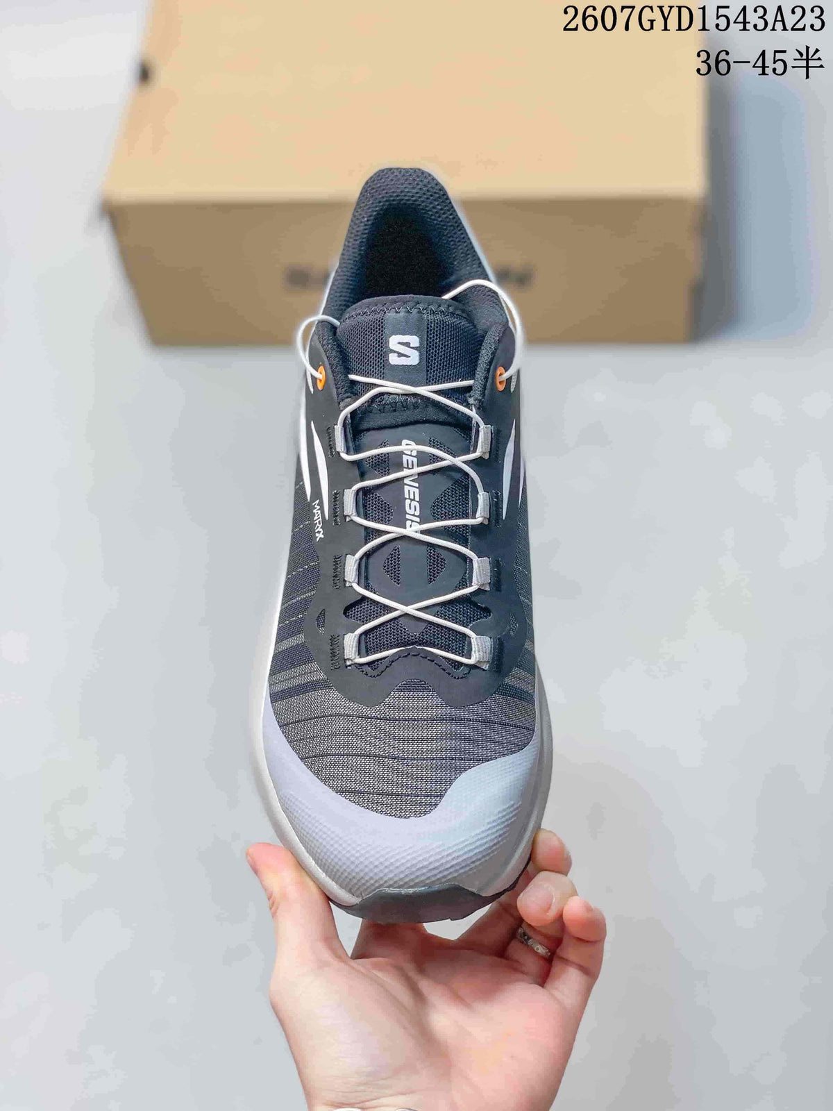 Top view showing the dark mesh-like upper, white laces, orange eyelet accents, and Salomon branding.