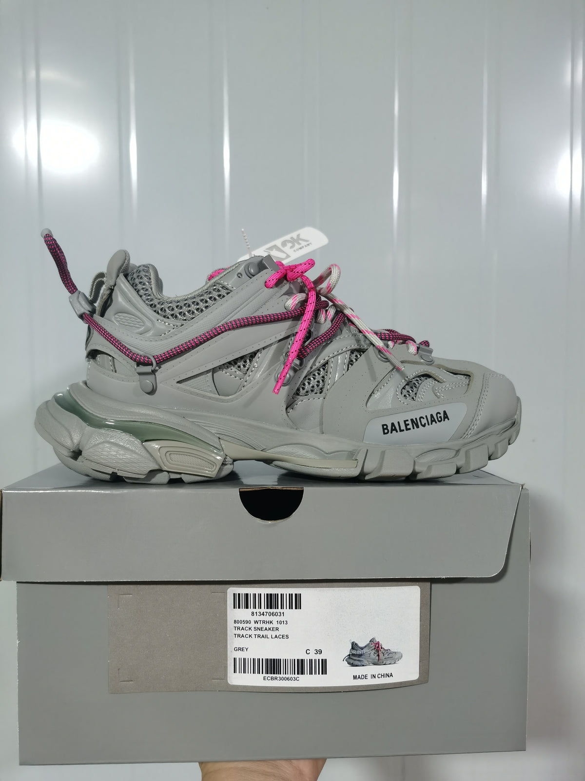 Side view of a grey Balenciaga Track sneaker with pink rope laces resting on its labeled shoe box.