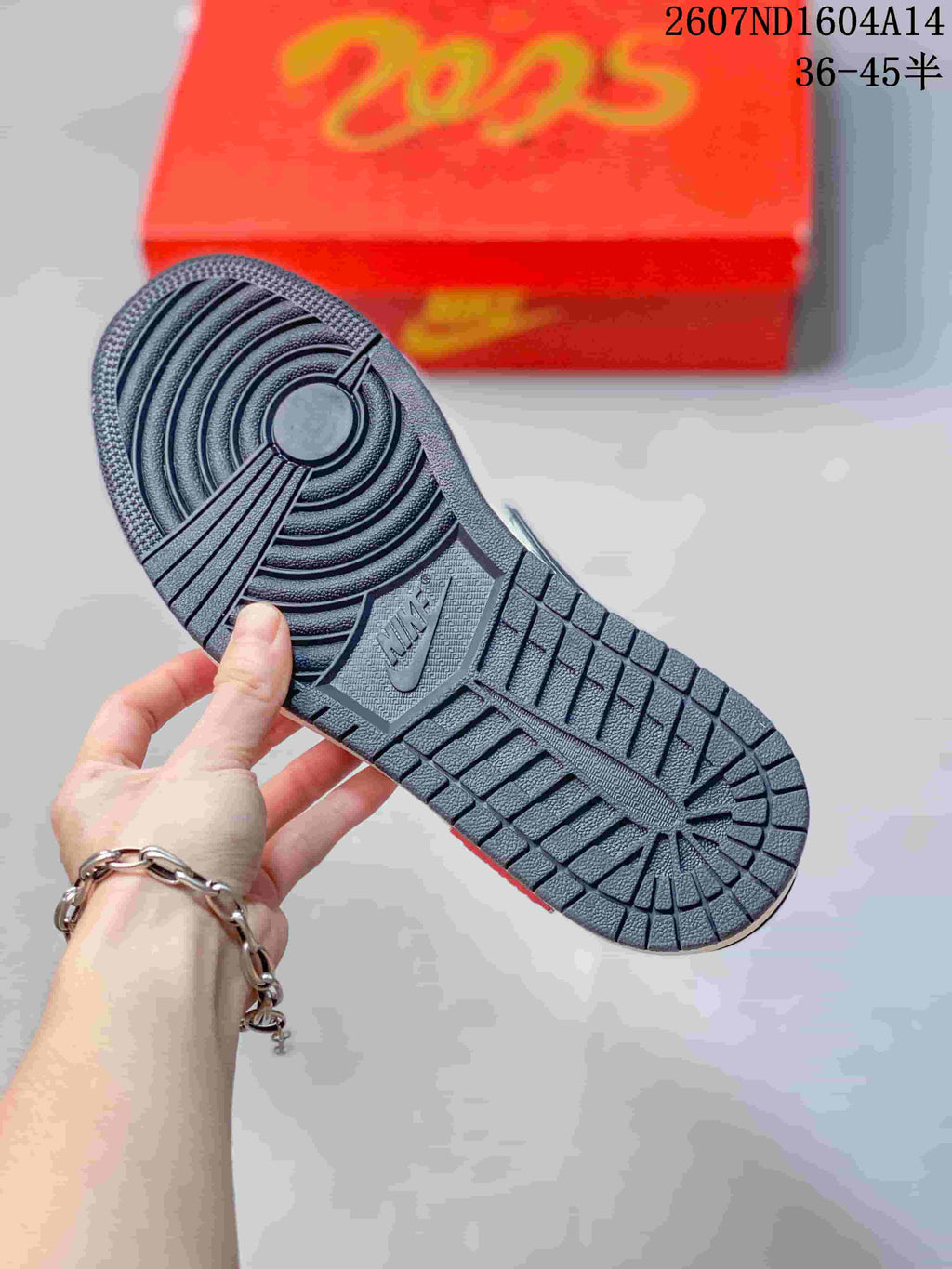 Close-up of the dark textured rubber outsole with circular and grid traction patterns; a red presentation box is in the background.