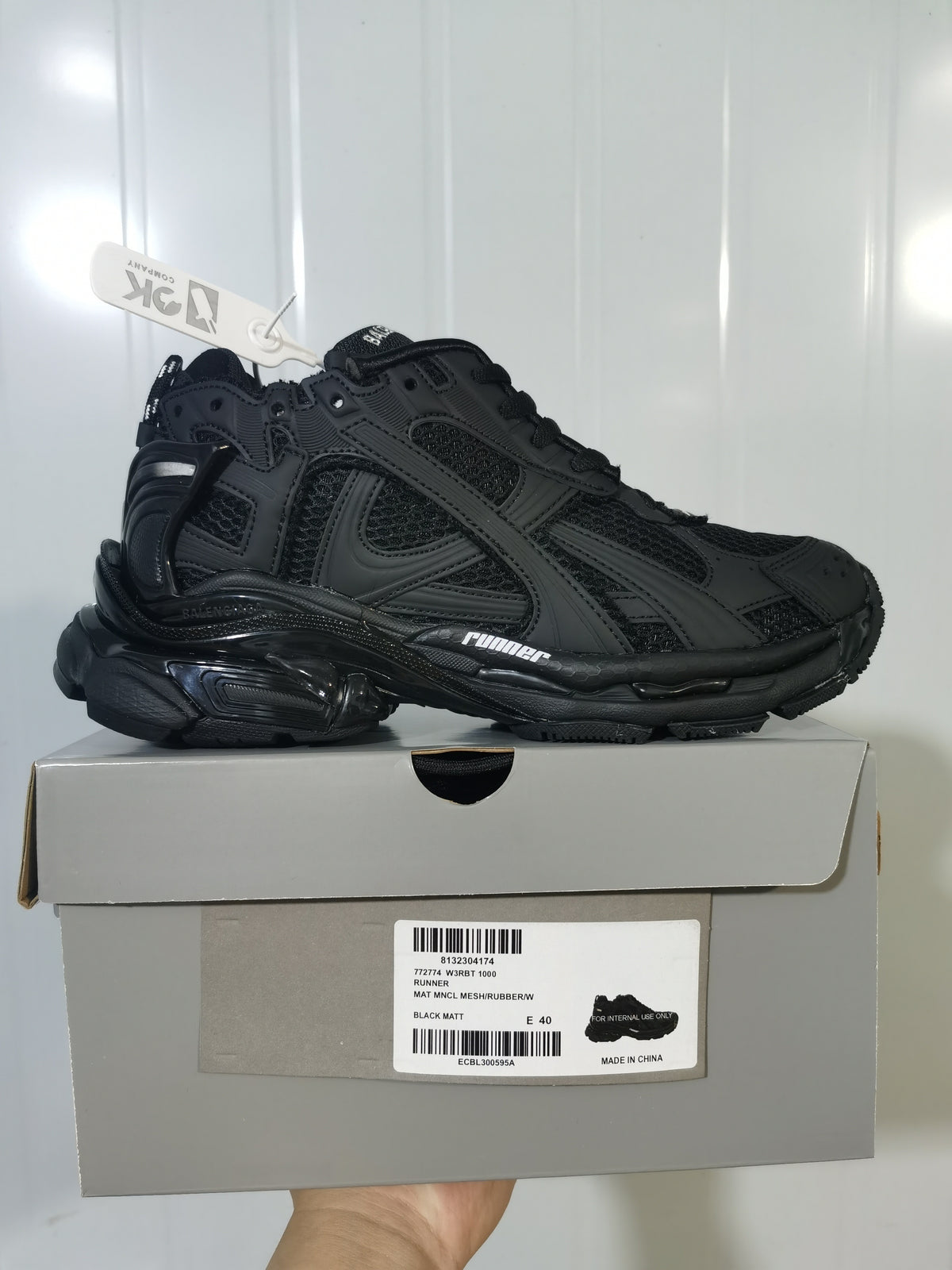 Side view of a black matte Balenciaga Runner sneaker resting on its shoe box; the box label shows RUNNER and a size 40 sample.