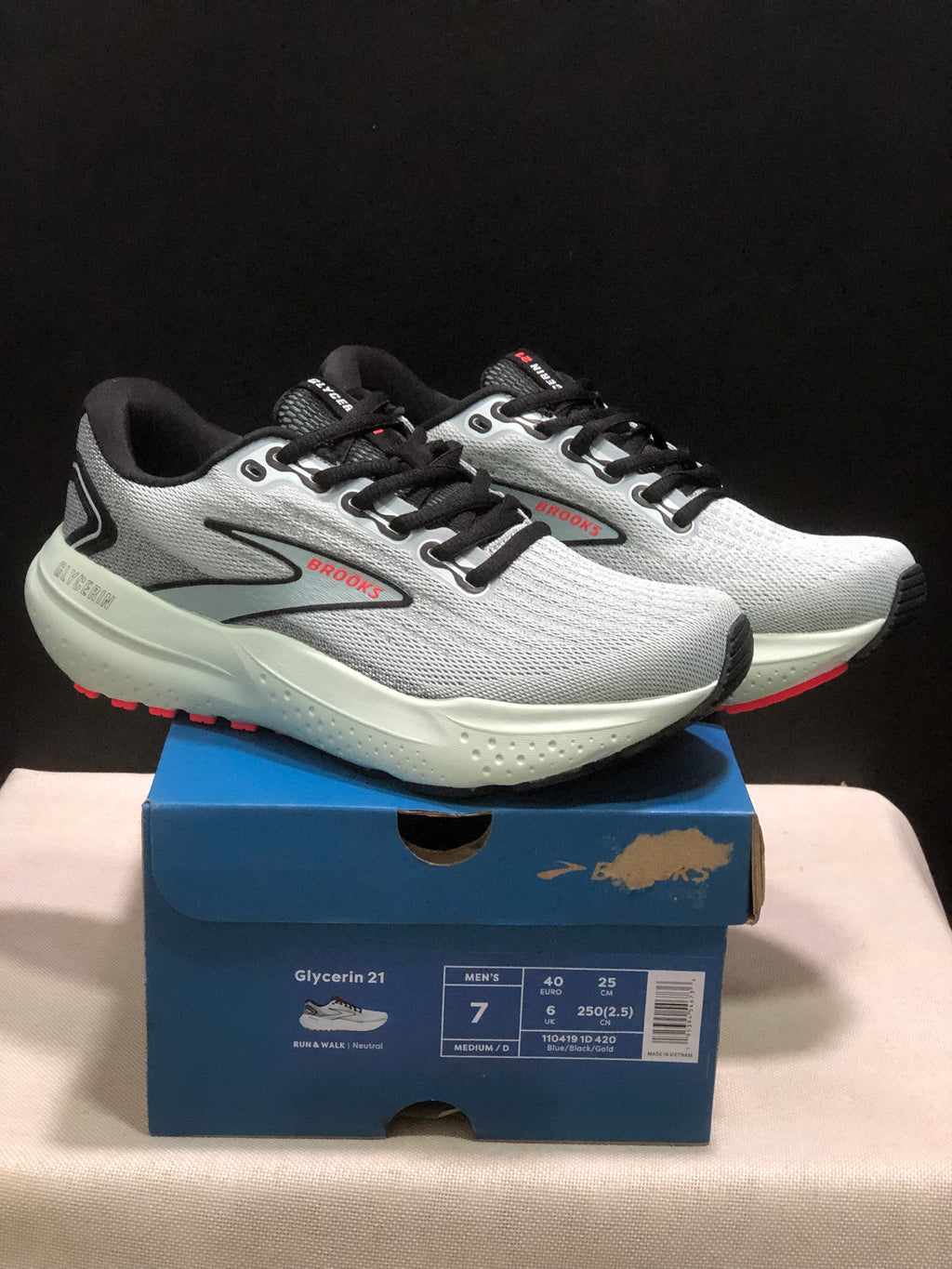 Pair of gray, black, and red Brooks Glycerin 21 sneakers displayed on a blue shoebox with a visible men's size label.