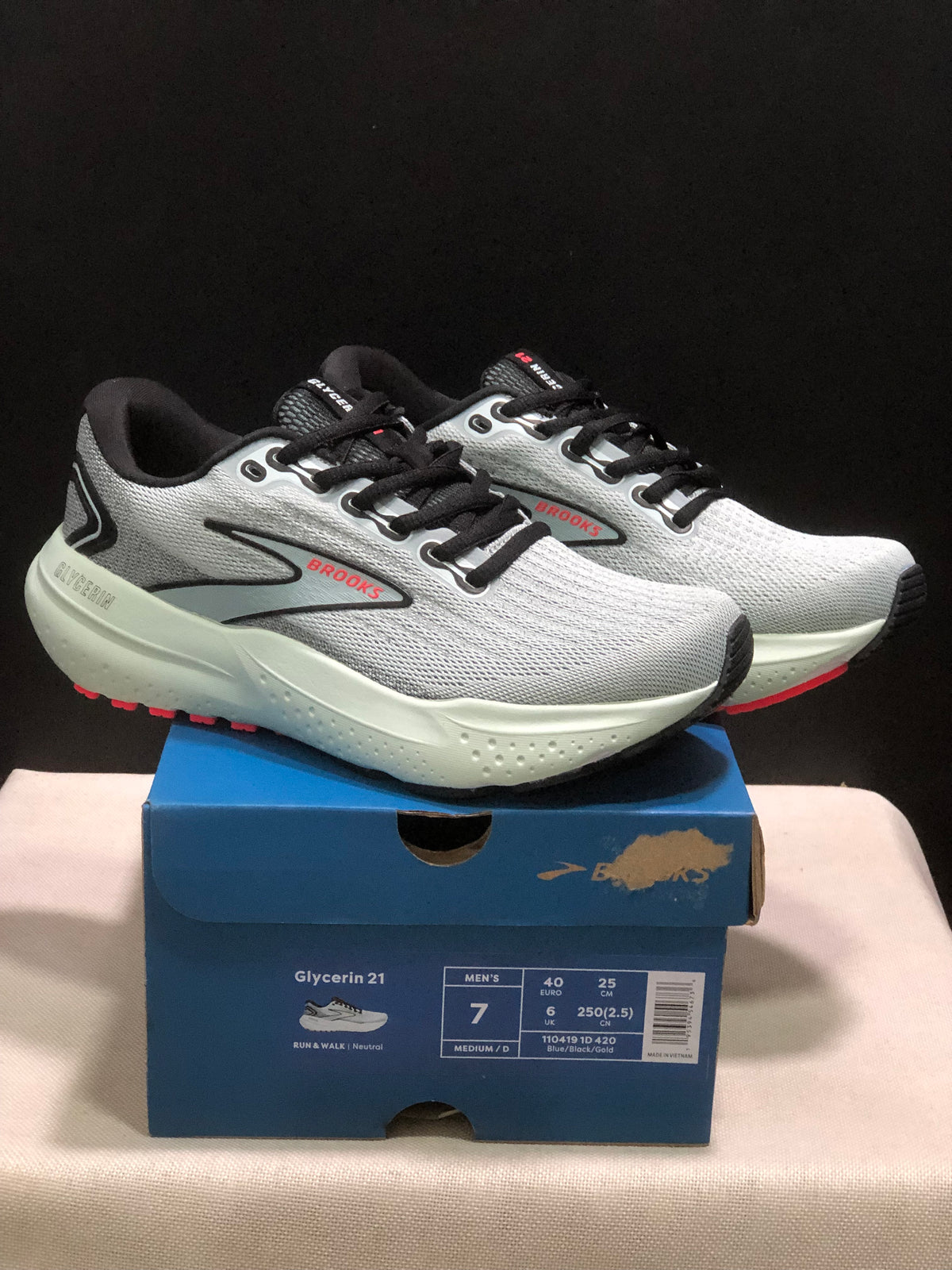 Pair of gray, black, and red Brooks Glycerin 21 sneakers displayed on a blue shoebox with a visible men's size label.