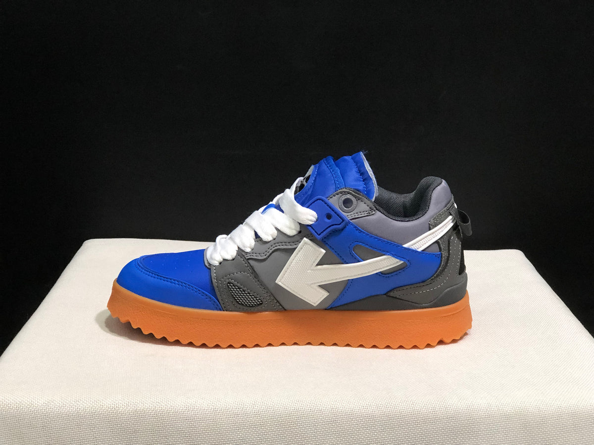 Side profile of one sneaker highlighting the blue overlay, grey upper panels, white arrow detail, and thick gum-colored sole.