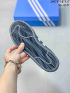 Close-up of the patterned outsole of a black Adidas Superstar sneaker with a blue Adidas shoebox in the background.
