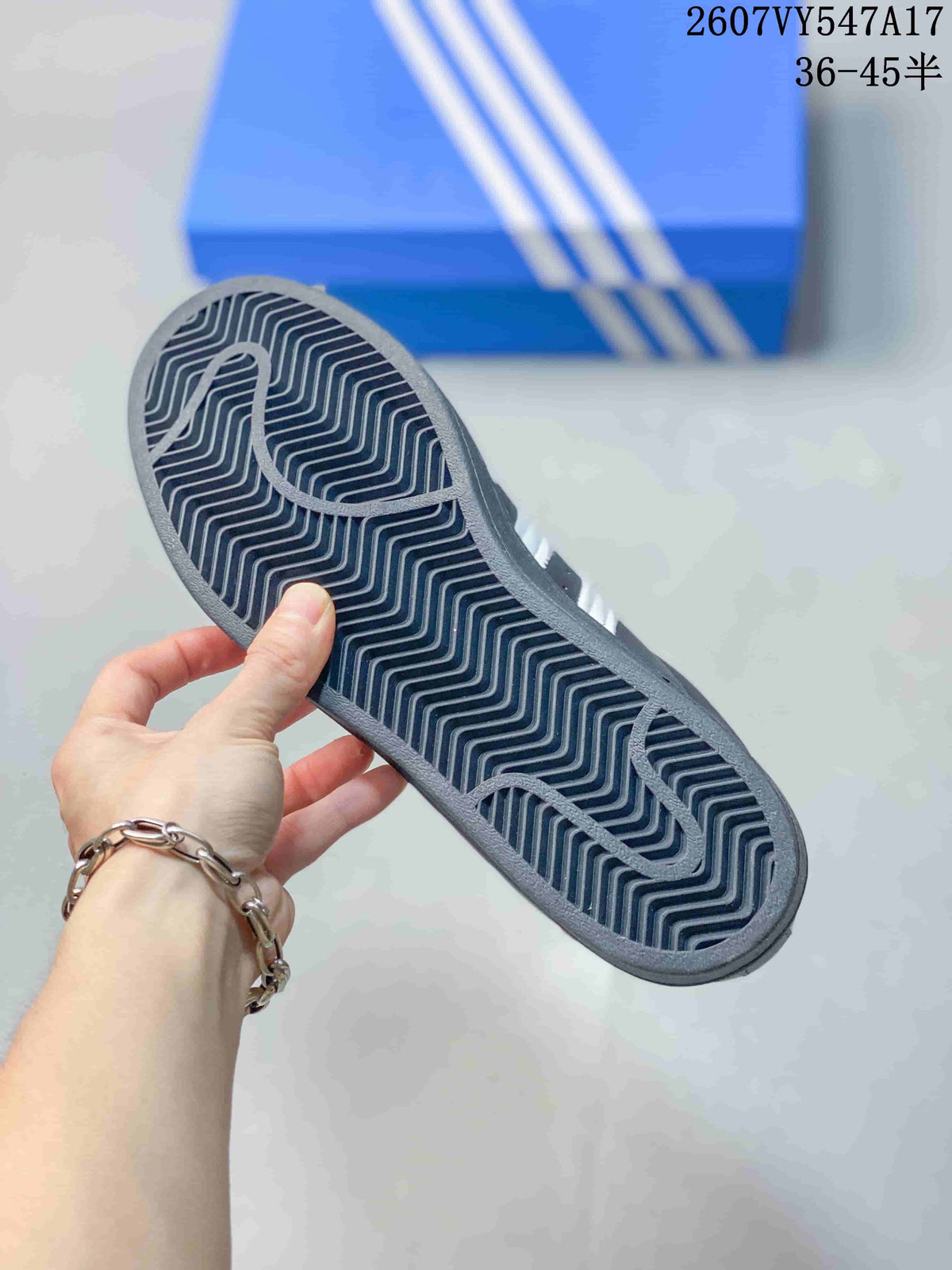 Close-up of the patterned outsole of a black Adidas Superstar sneaker with a blue Adidas shoebox in the background.