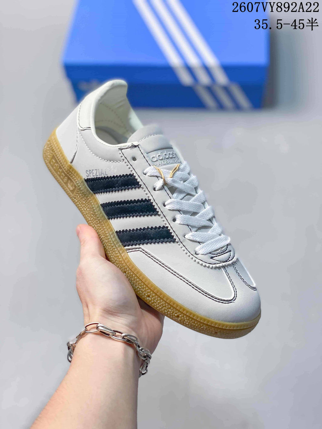 Close side view of a white adidas sneaker with dark blue stripes, lace-up front, gum sole, and visible Spezial branding.