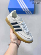 Close side view of a white adidas sneaker with dark blue stripes, lace-up front, gum sole, and visible Spezial branding.