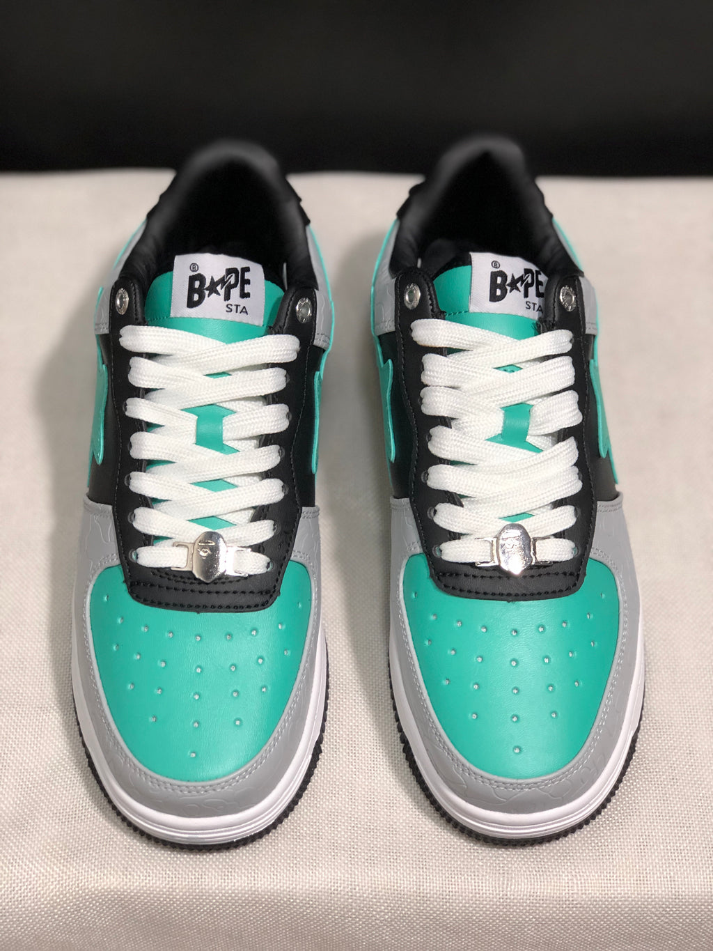 Front top view showing the turquoise toe boxes, white laces, tongue branding and metallic lace hardware.