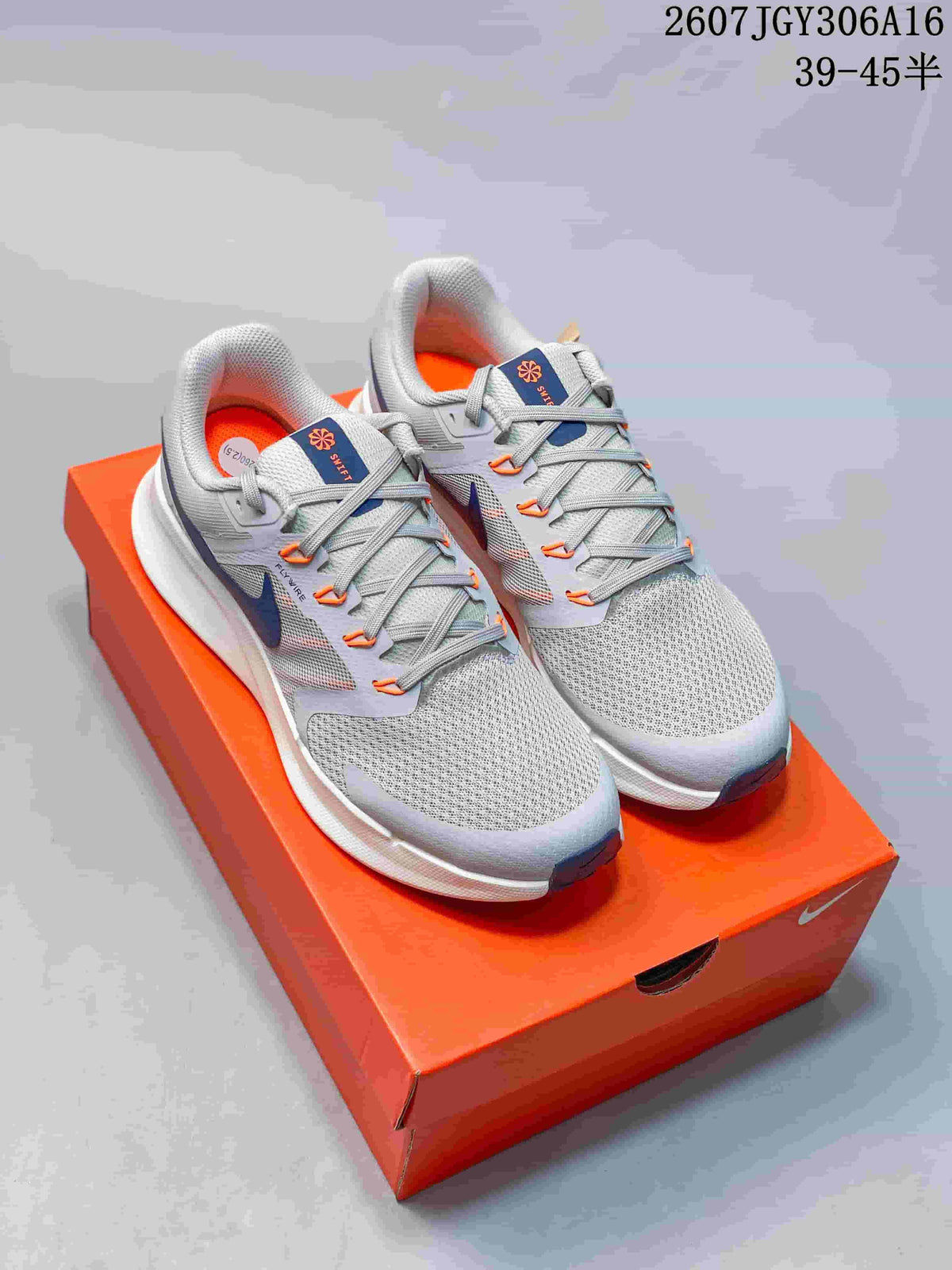 Pair of gray Nike Run Swift 3 sneakers with navy and orange accents displayed on an orange shoe box.