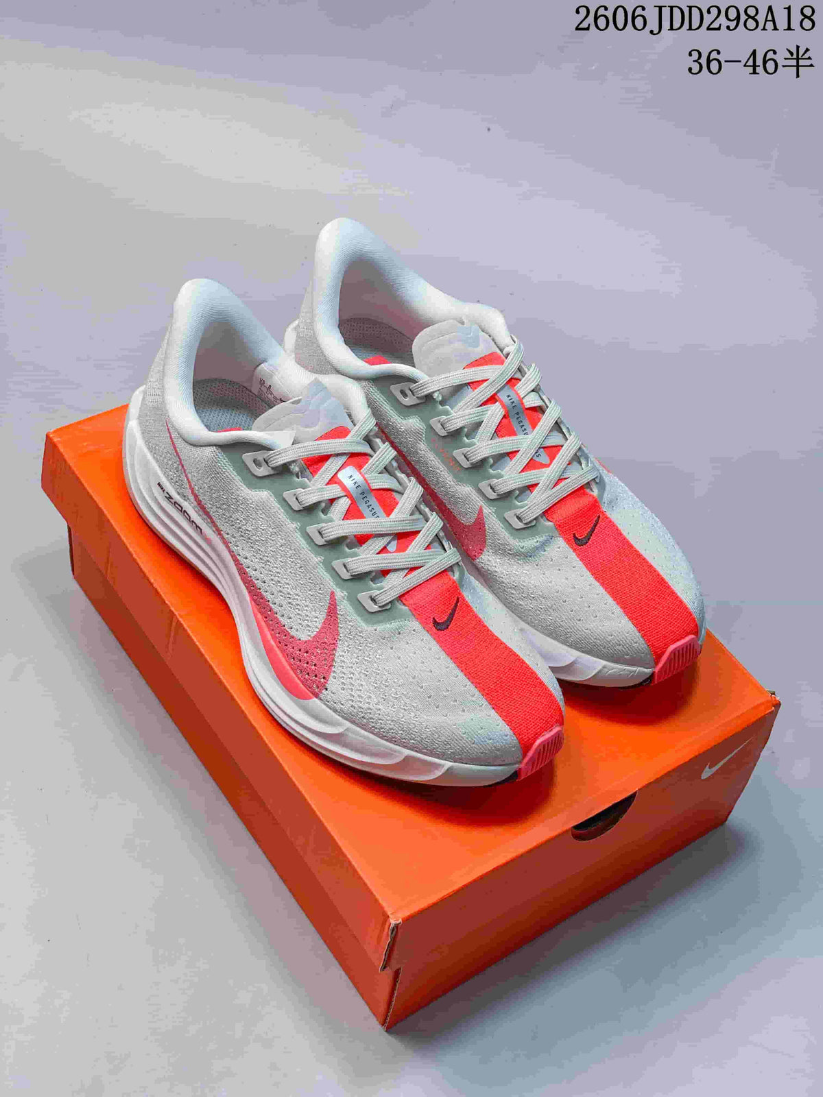 Pair of light grey and red Nike ReactX Pegasus Plus Next Nature sneakers displayed on an orange Nike shoebox.