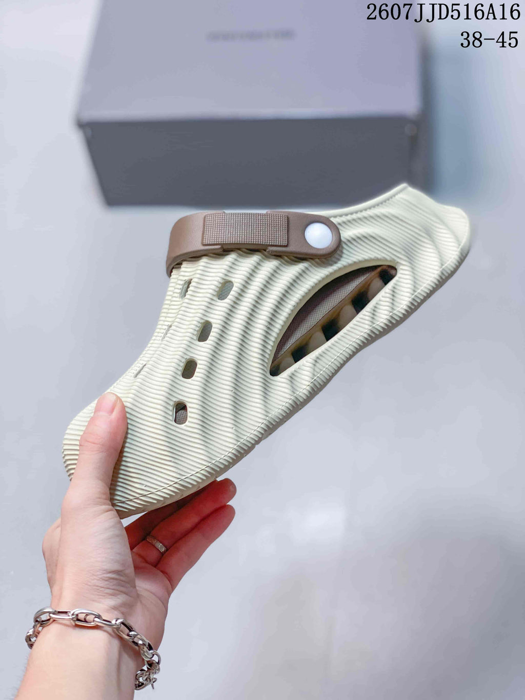 Side view of a cream clog slide showing the ribbed upper, side ventilation opening, and adjustable brown heel strap.