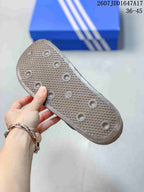 Close-up of the textured outsole of a black adidas slide, showing a crosshatch pattern and raised circular traction details.
