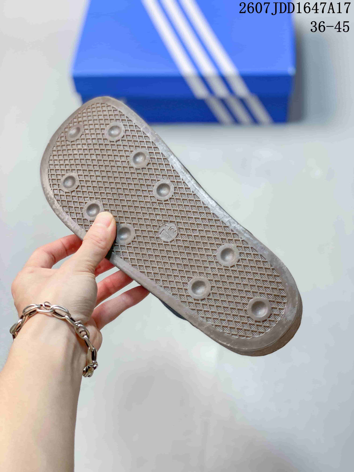 Close-up of the textured outsole of a black adidas slide, showing a crosshatch pattern and raised circular traction details.