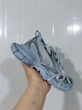 Cyan blue chunky sneaker held at an angled side view, showing layered panels, black contrast detailing and matching laces.