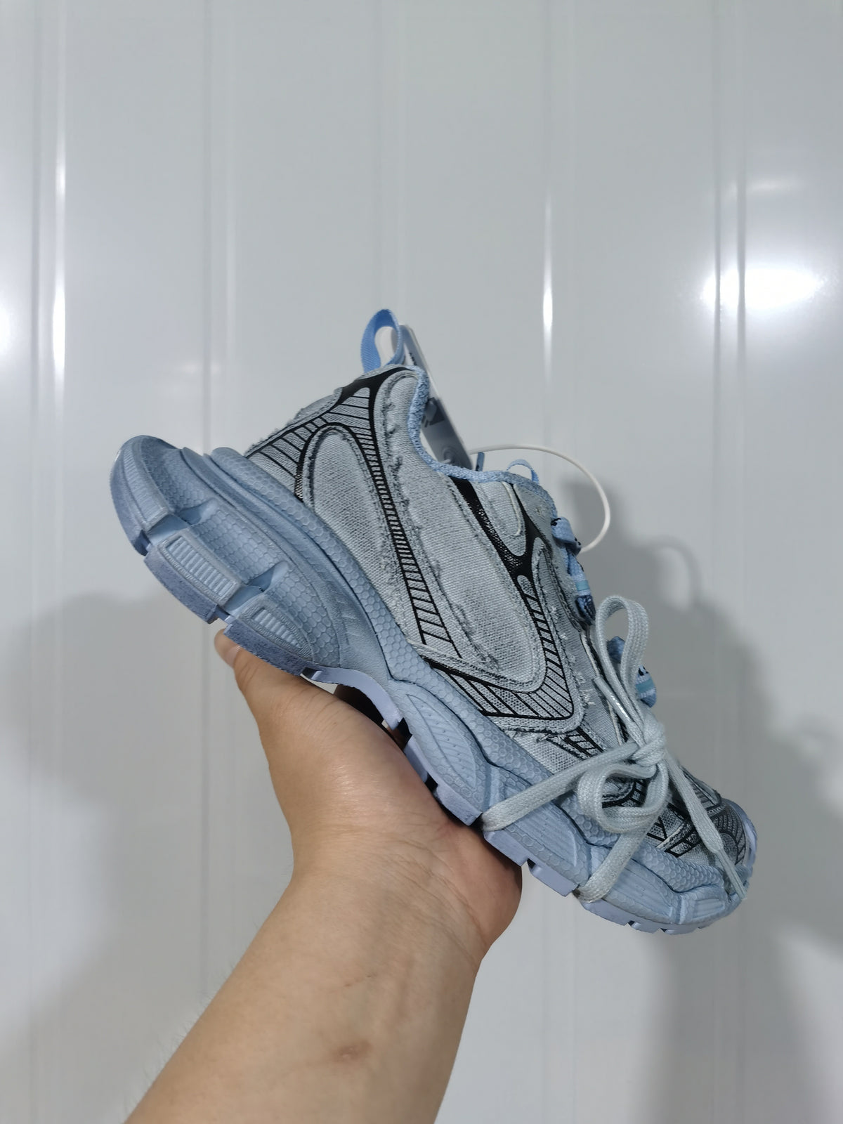 Cyan blue chunky sneaker held at an angled side view, showing layered panels, black contrast detailing and matching laces.