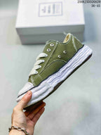 Side view of an olive low-top sneaker showing contrast stitching, metal eyelets, dark trim, and a sculpted white outsole.