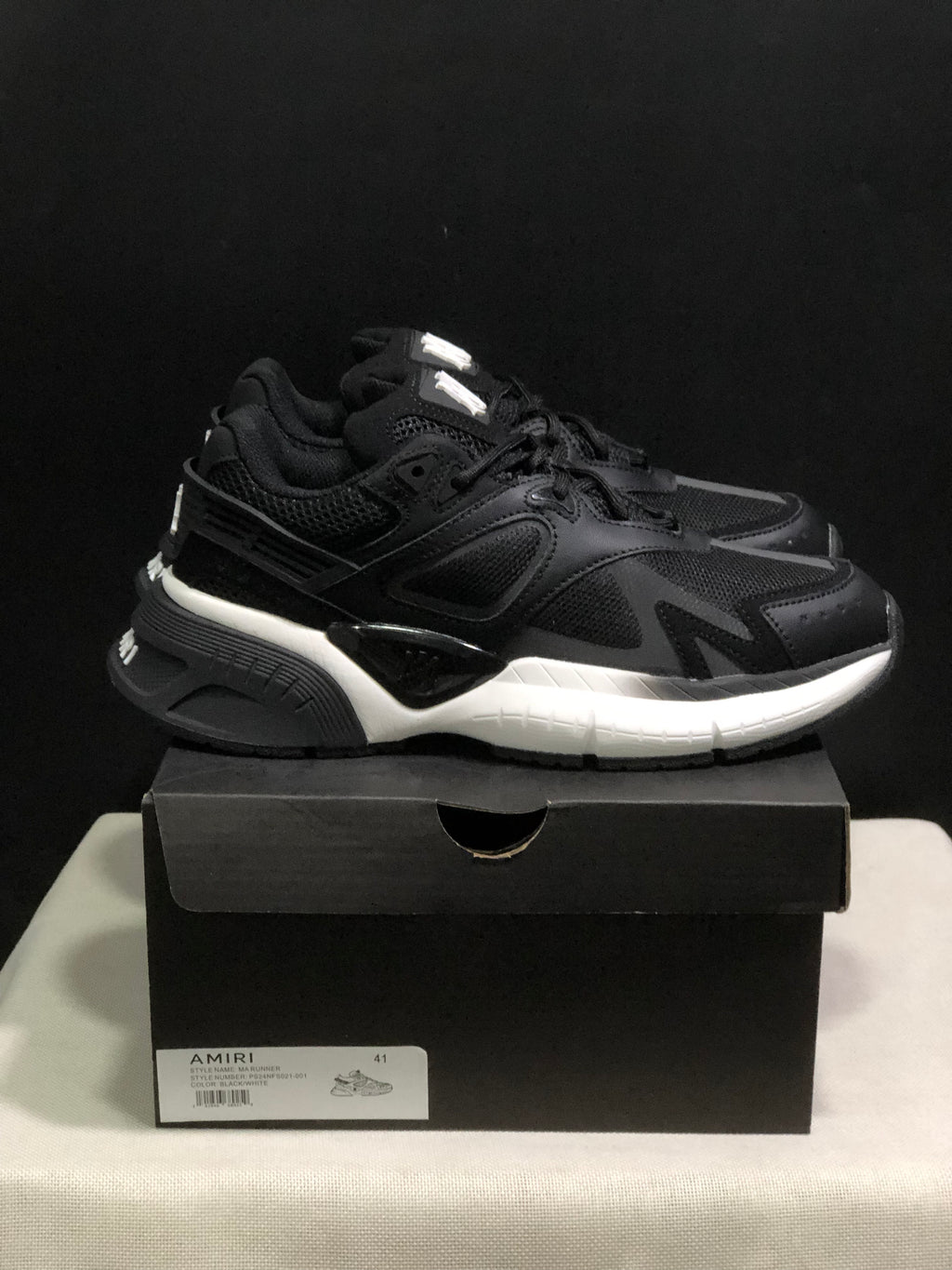 Side view of the black and white AMIRI MA Runner sneakers showing layered panels, mesh sections, and a contrasting white midsole.