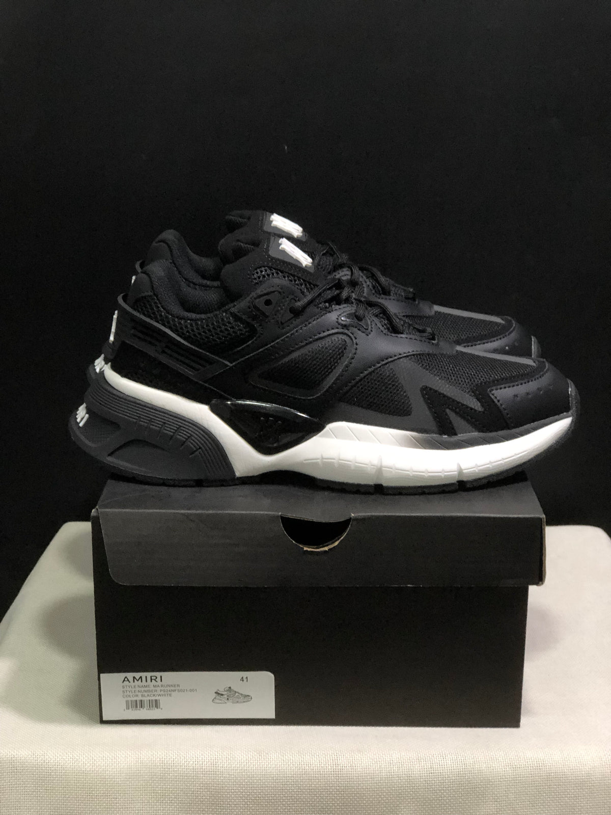 Side view of the black and white AMIRI MA Runner sneakers showing layered panels, mesh sections, and a contrasting white midsole.