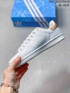 Side profile showing the white upper, perforated stripe detail, gold heel accent and textured sole.