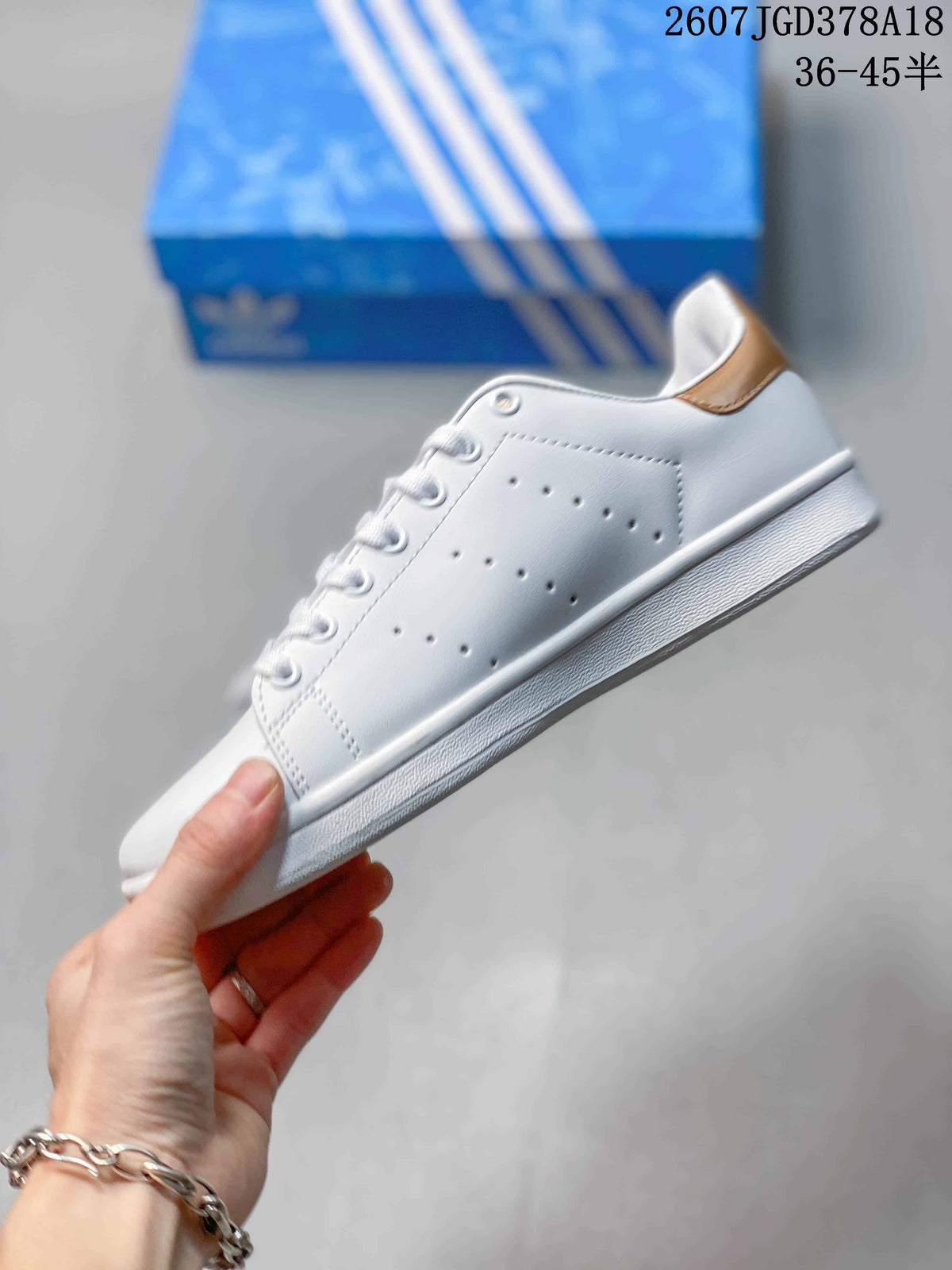 Side profile showing the white upper, perforated stripe detail, gold heel accent and textured sole.