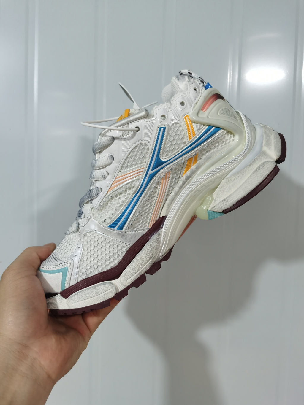 Side and outsole view of the Balenciaga Runner sneaker showing blue and yellow overlays, burgundy trim, and a contrasting rubber tread.