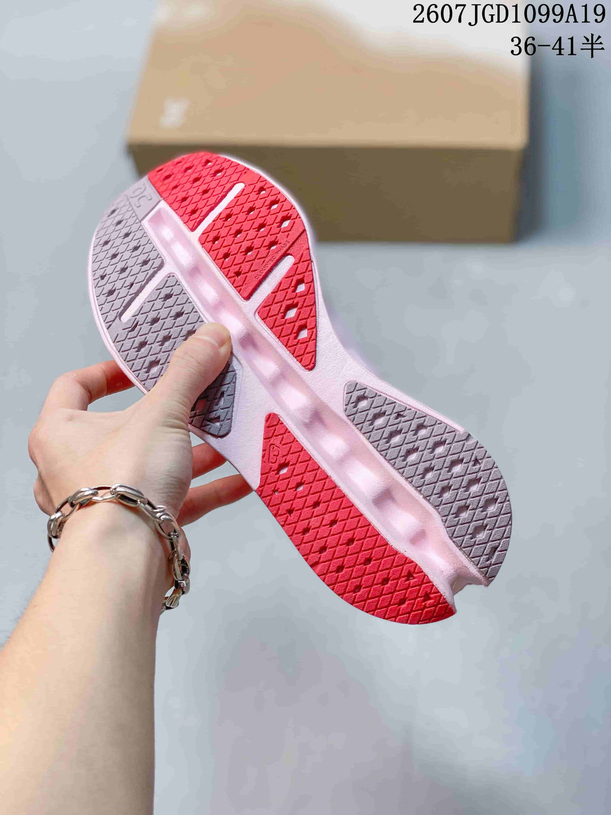 Close view of the sneaker outsole showing pink, red and gray tread sections with geometric traction patterns.