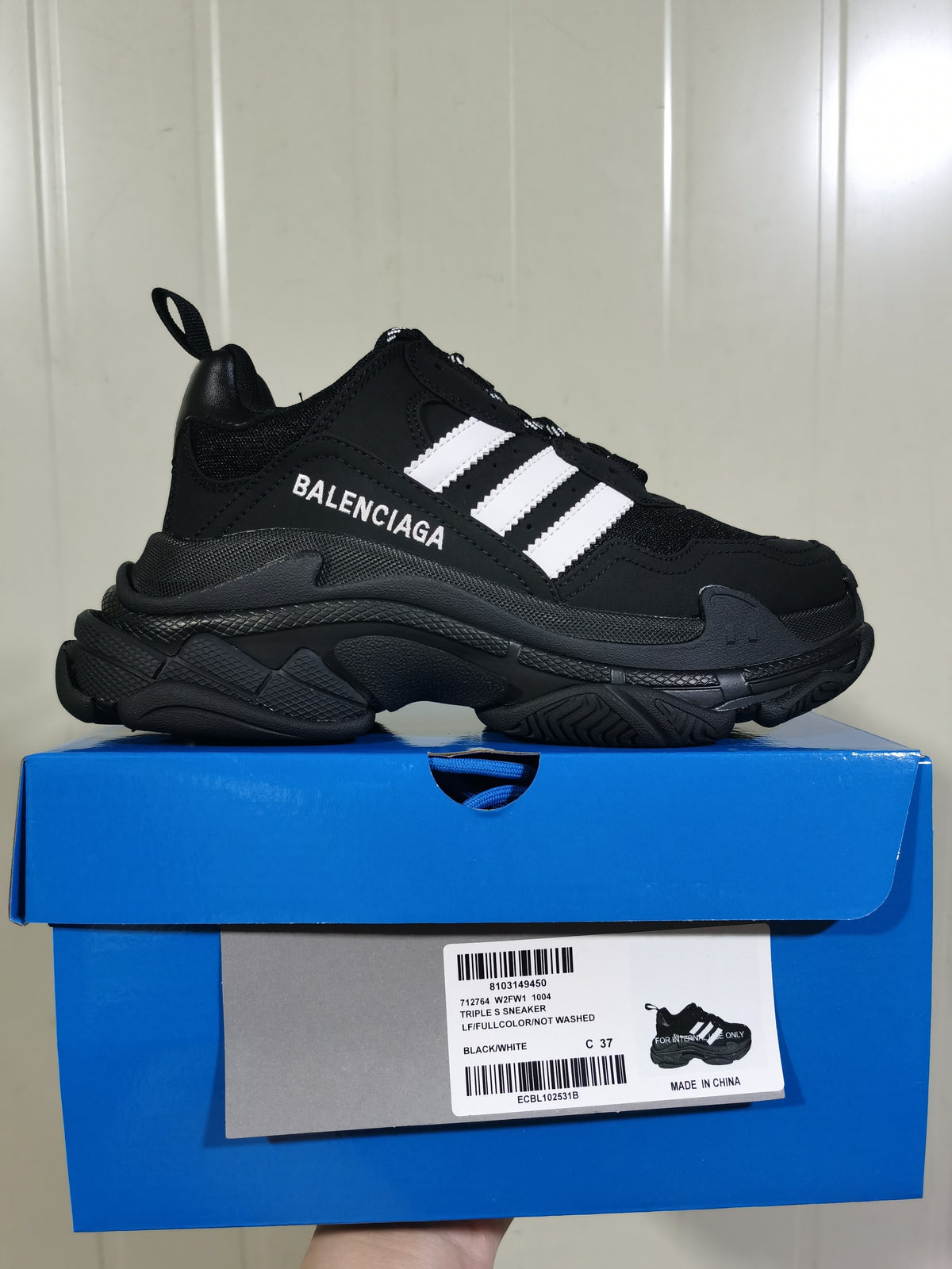 Black and white Balenciaga Triple S sneaker displayed on its blue shoe box, with the box label showing style code 712764 W2FW1 1004 and sample size C 37.