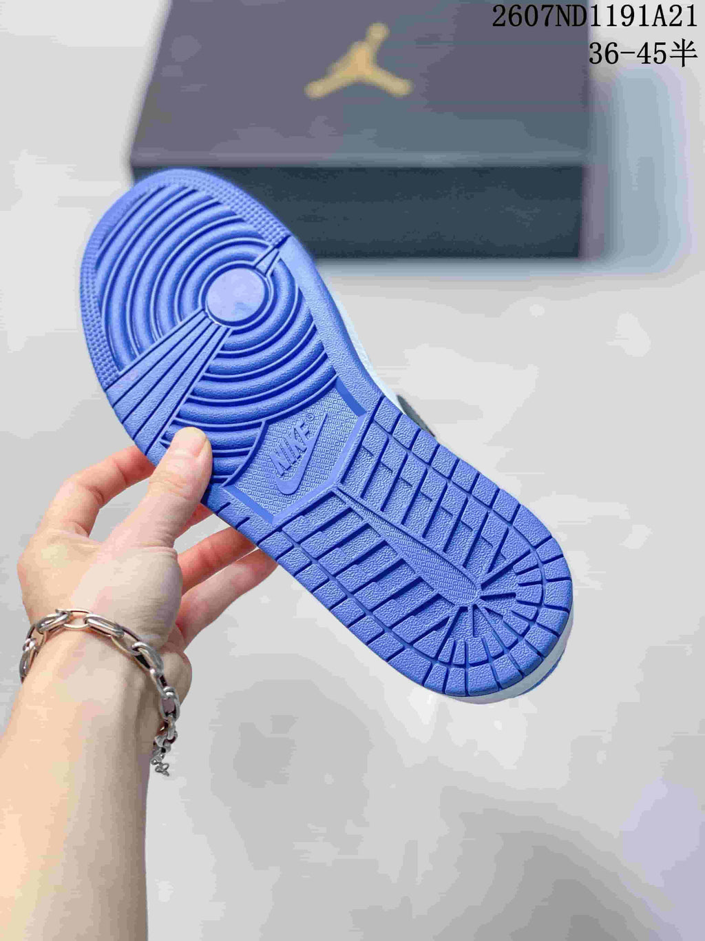 Blue rubber outsole held above a Jordan shoebox, showing circular and grid traction patterns.