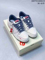 Pair of white Nike Dunk Low sneakers with dark navy patterned laces and red tongue labels, displayed on a shoebox.