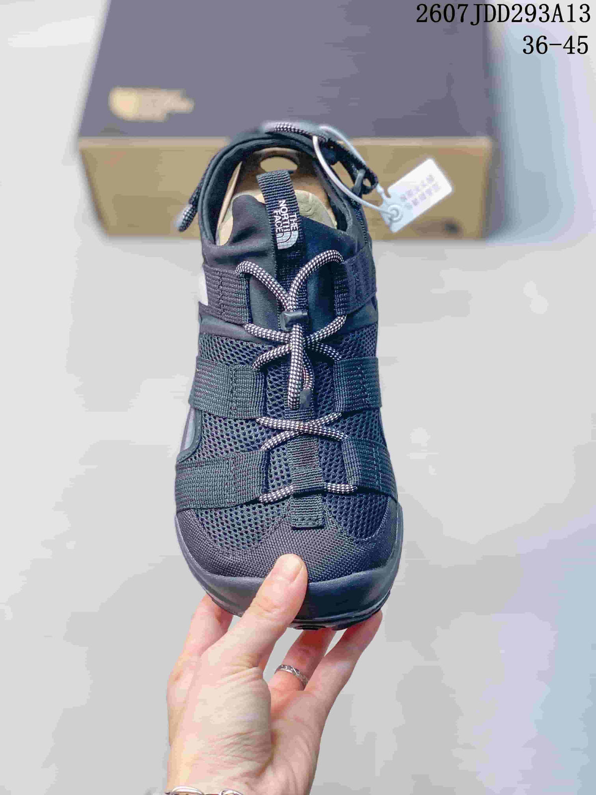 Front view of a black sandal showing the covered toe, mesh upper, multiple straps, and toggle lace.