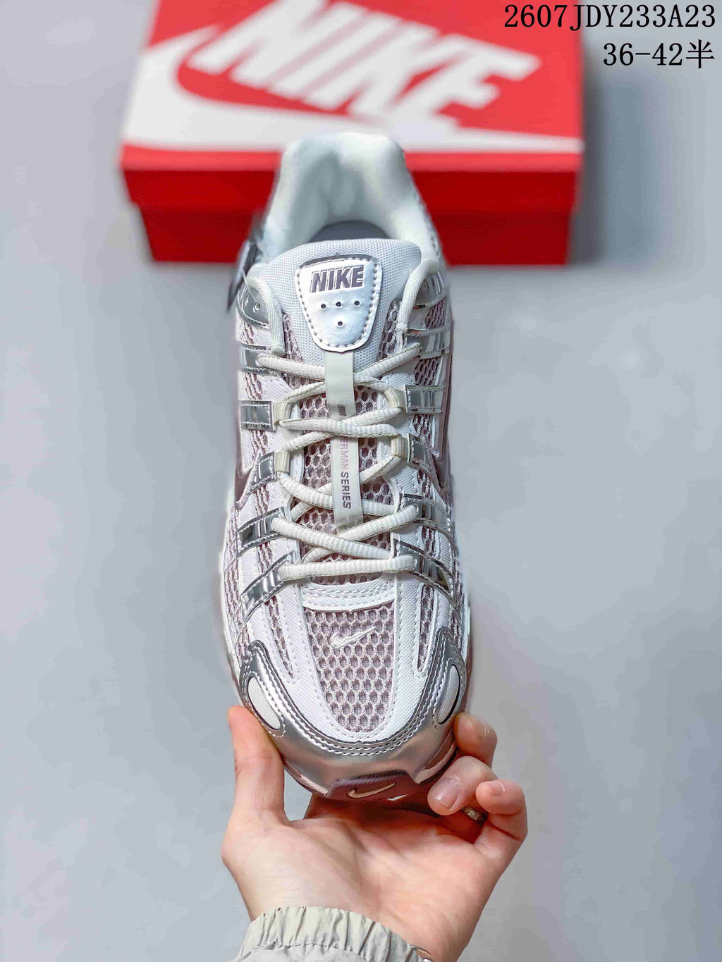 Top-down view of a silver and white Nike sneaker showing the lace-up construction, mesh-look tongue, and layered toe design; size range 36–42.5 is visible.