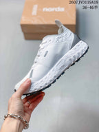 Side view of the white NORDA sneaker showing gray detailing, orange accents, layered upper panels, and a rugged outsole.