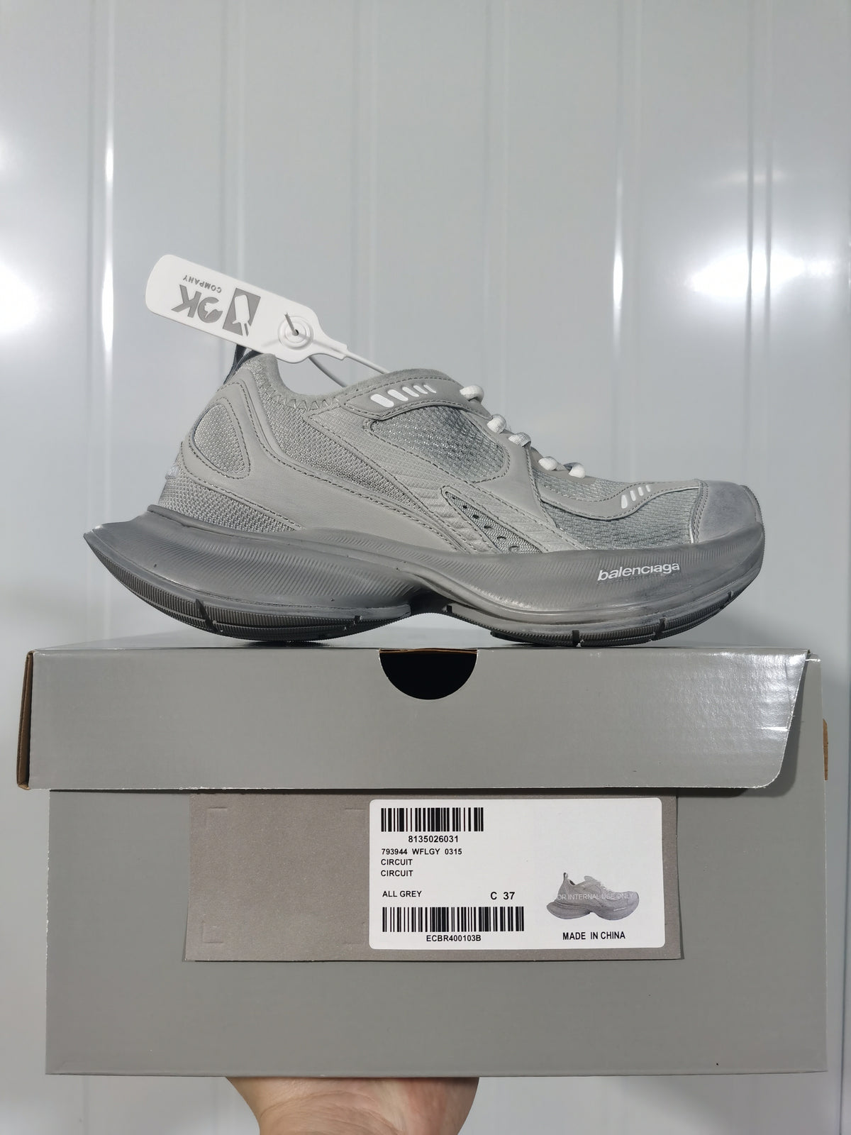 Side view of a grey Balenciaga sneaker resting on its box, with the box label showing Circuit, All Grey, style code 0315 and size C 37.
